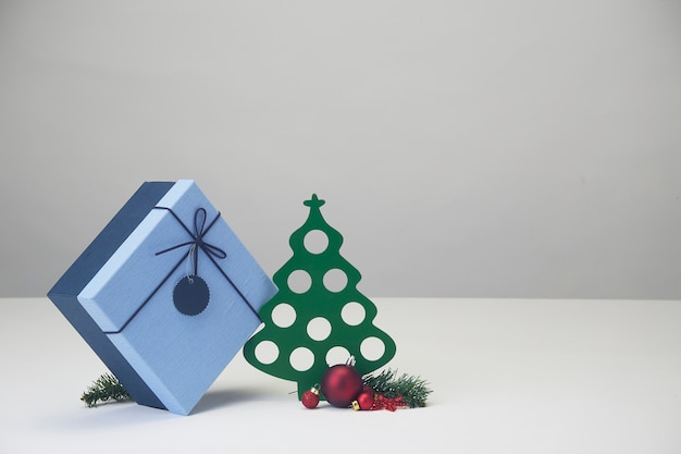 Украшенные елочные шары и елка с подарочной коробкой на белом столе