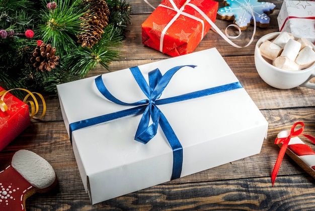 Decorated Christmas gifts boxes on a wooden table, with a cup of hot chocolate, gingerbread and Christmas tree branches. Copy space