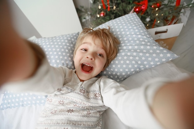 Photo decorated christmas tree stands in the room near the bed on which the child lies