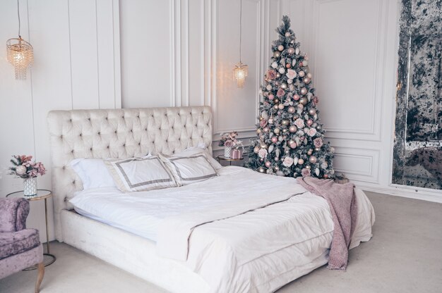 Decorated Christmas tree in white classic bedroom interior 