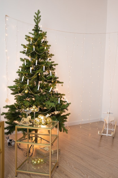 Decorated christmas tree over white wall with copy space. Christmas tree with golden decorations, festive interior.