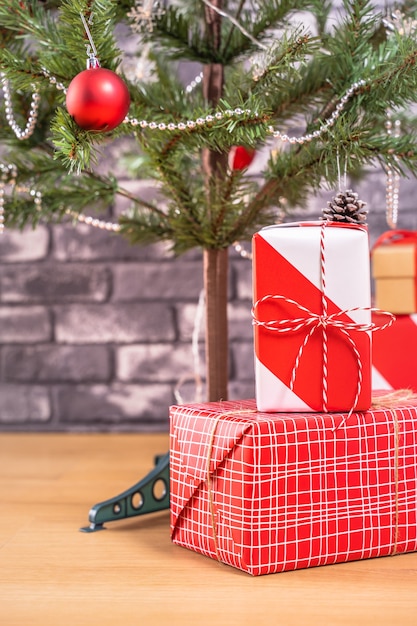 Decorated Christmas tree with wrapped beautiful red and white gifts at home with black brick wall, festive design concept, close up.