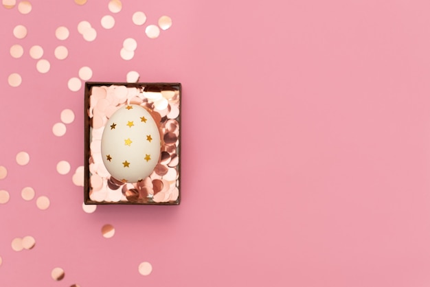 Decorated easter egg with party streamers on pink background. 