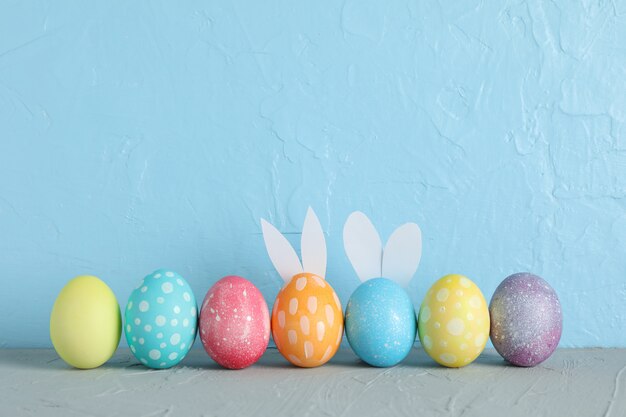 Uova di pasqua decorate e le orecchie del coniglietto sveglio sulla tavola contro il fondo di colore