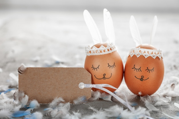 Decorated Easter eggs and cute bunny's ears with empty tag on gray table with white feathers