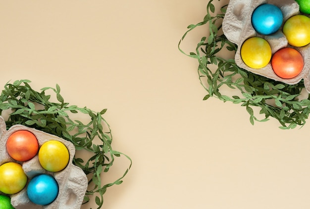 Decorated Easter eggs lie in the carton box on yellow with green leaves