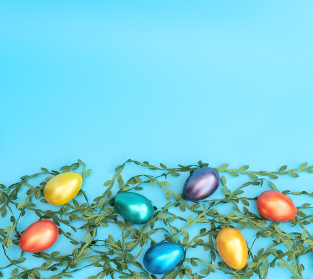 Украшенные пасхальные яйца лежат на зеленых листьях на синем