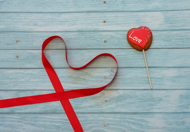 Decorated heart shape cookie on a stick with red tape in form of heart on blue wooden background. Space for text. Concept Valentines day. Love