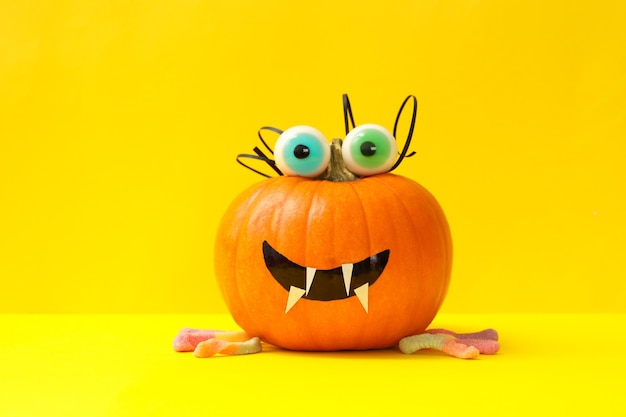 Decorated pumpkin with candy eyes on yellow background