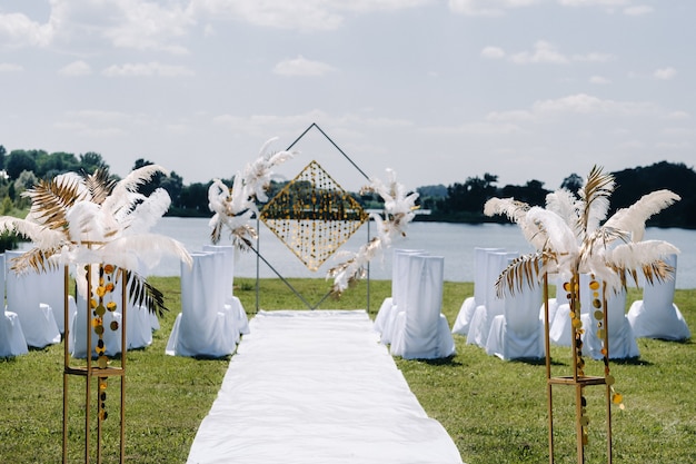 Decorated wedding arch in nature.Wedding ceremony with an arch decorated with retro-style feathers on a lake background