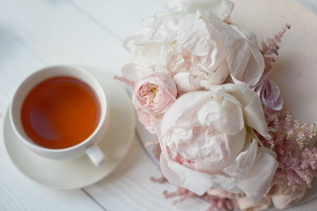 Foto decorato con fiori freschi, una torta bianca nuda, una torta elegante per matrimoni ed eventi una tazza bianca con una bevanda calda