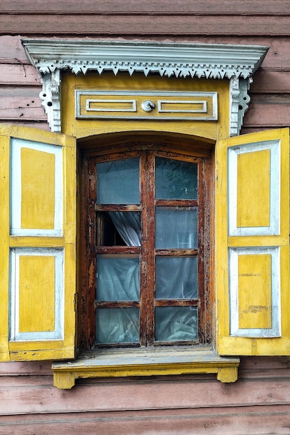 Decorated with ornamental carvings windows with shutters frames on vintage wooden rural house in IrkutskRussia Russian traditional national folk style in wooden architecture Countryside Landmark