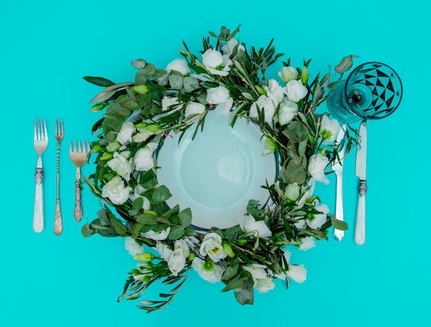 Decorated wreath with white roses and cutlery on green background. Decorated. Above view