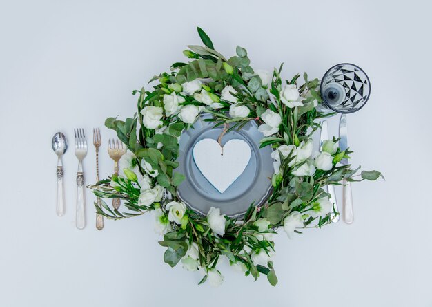 Decorated wreath with white roses and cutlery on white background. Decorated. Above view