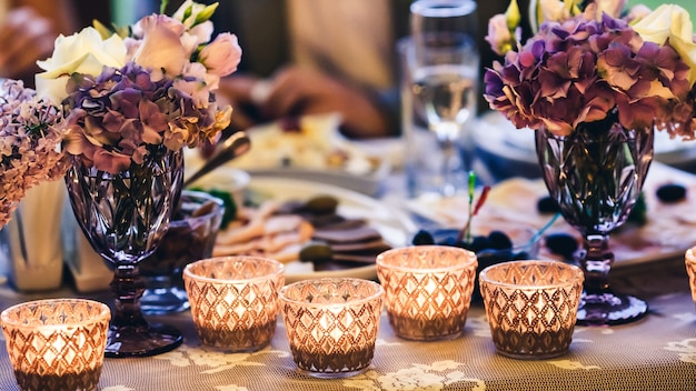 Decoratie op tafel kaarsen in glazen, paarse bloemen in vazen