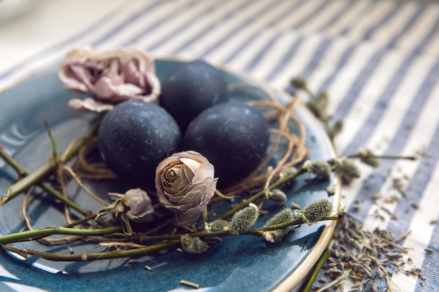 Decoratieontwerp blauwe paaseieren liggen op een bord met een wilg op een gestreepte stoffenachtergrond