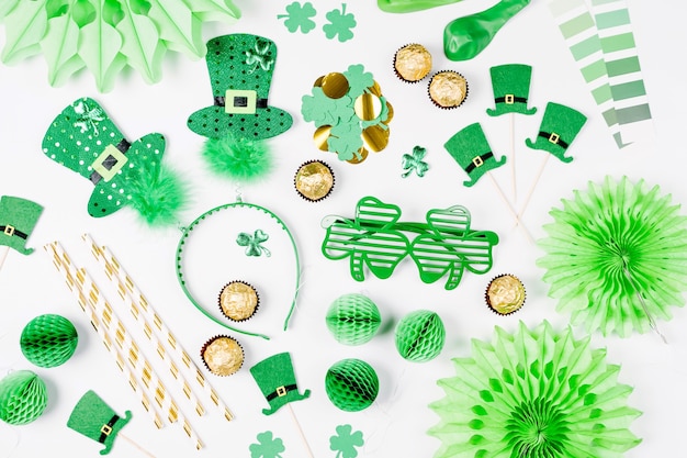 Decoraties en rekwisieten voor St.Patrick's Day-feest. Groene en gouden papieren versieringen, haar hoepel met hoeden, klaverblad, zonnebril, ballonnen, confetti en snoep op witte achtergrond. Platliggend, bovenaanzicht