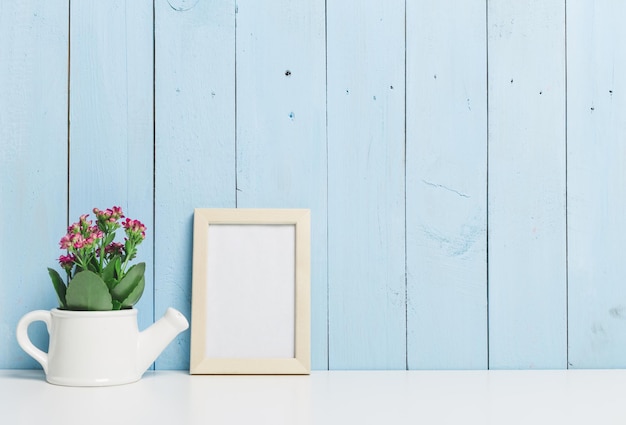 Decoratieve binnenomgeving met een plantenwaterpot en een leeg frame tegen een blauwe houten muur