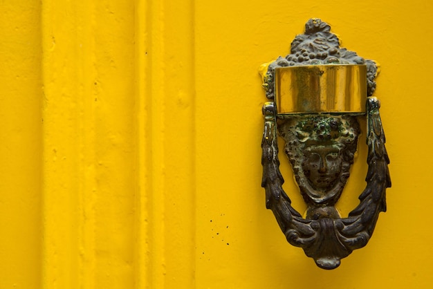 Foto decoratieve bronzen deurklopper in de vorm van een mooi vrouwelijk hoofd op een gele geschilderde deur
