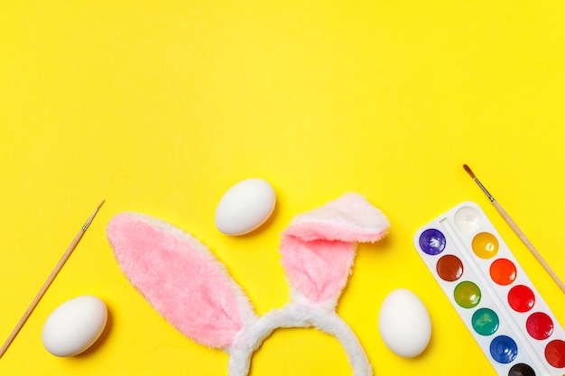 Decoratieve eieren kleurrijke verf en konijnenoren harige kostuum speelgoed geïsoleerd op trendy gele achtergrond