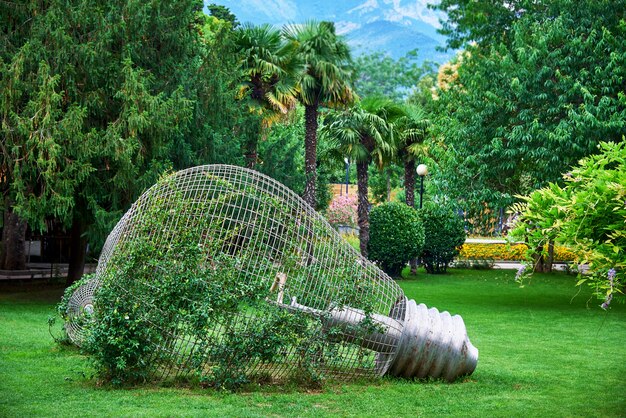 Decoratieve gloeilamp in levende planten op een gazon met dikke bomen en struiken.