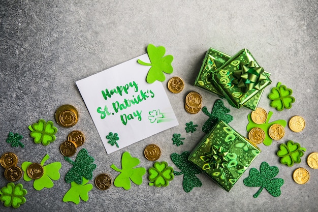 Decoratieve klaverblaadjes, groene geschenkdoos, munten op stenen achtergrond, plat leggen. St. Patrick's Day-viering. Kaart Gelukkige St. Patrick Dag