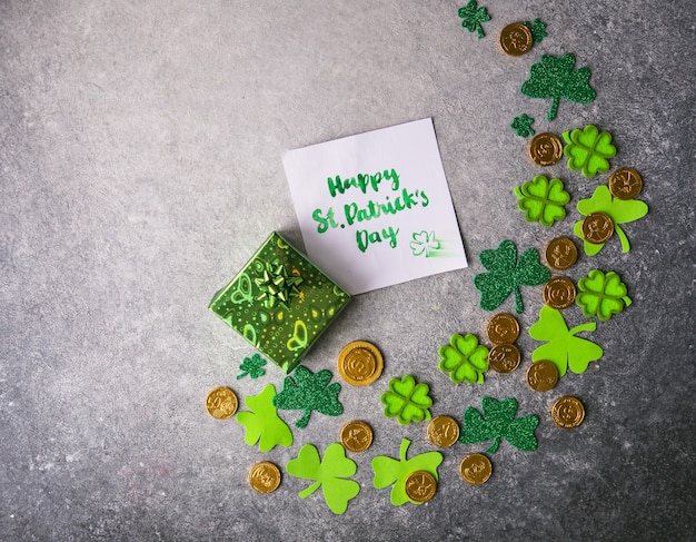 Decoratieve klaverblaadjes, groene geschenkdoos, munten op stenen achtergrond, plat leggen. St. Patrick's Day-viering. Kaart Gelukkige St. Patrick Dag