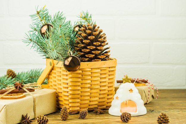 Decoratieve rieten mand met groene sparren takken, ballen en ceder kegel. geschenkdozen en een kaars in een kandelaar op een houten tafel.