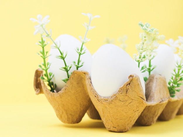 Decoratieve witte eieren in een kartonnen doos met lentebloemen op geel