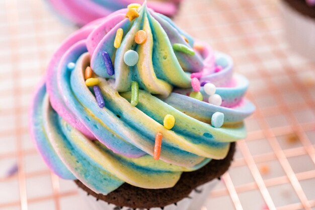 Decorating chocolate unicorn cupcakes with colorful buttercream icing and sprinkles.