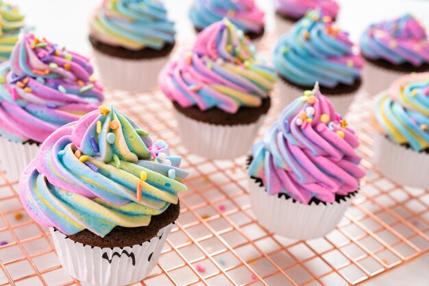 Photo decorating chocolate unicorn cupcakes with colorful buttercream icing and sprinkles.