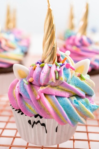 Decorating chocolate unicorn cupcakes with colorful buttercream icing and sprinkles.