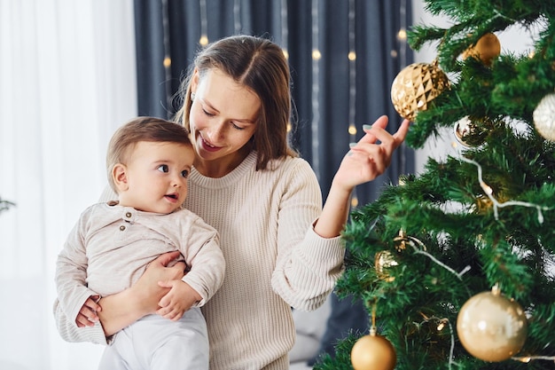 クリスマス ツリーを飾る母と彼女の小さな娘は家で一緒に室内で
