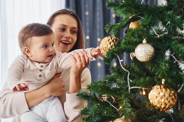 Decorating Christmas tree Mother with her little daughter is indoors at home together