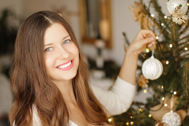 クリスマスツリーと冬の休日のコンセプトを飾るお祝いの飾りを保持している幸せな笑顔の女性...