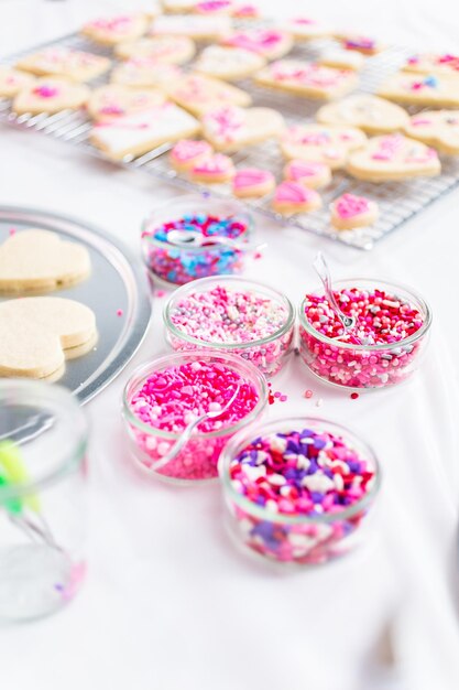 Decorating heart shape sugar cookies with royal icing and pink sprinkles for Valentine's day.