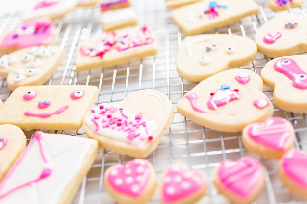 Decorating heart shape sugar cookies with royal icing and pink sprinkles for Valentine's day.