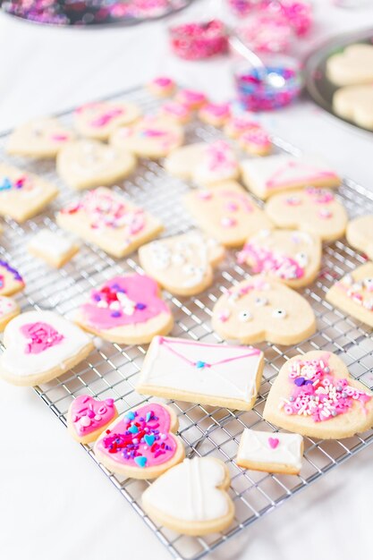 Decorating heart shape sugar cookies with royal icing and pink sprinkles for Valentine's day.