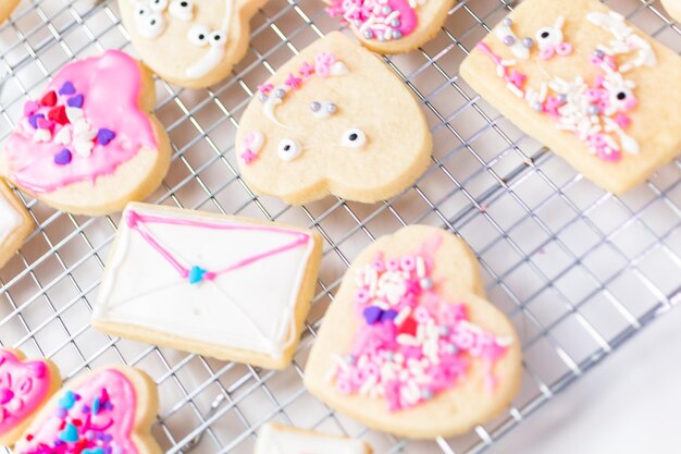 Decorating heart shape sugar cookies with royal icing and pink sprinkles for Valentine's day.