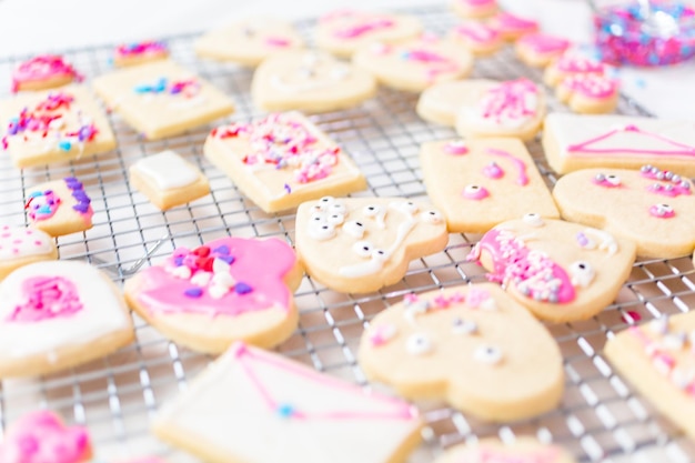 Decorating heart shape sugar cookies with royal icing and pink sprinkles for Valentine's day.