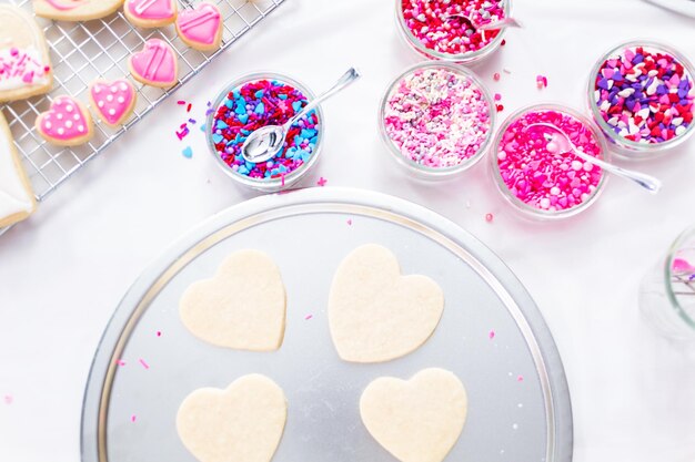 Decorating heart shape sugar cookies with royal icing and pink sprinkles for Valentine's day.