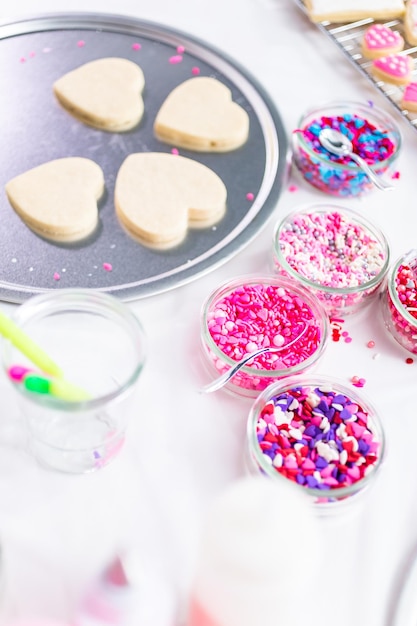 Decorating heart shape sugar cookies with royal icing and pink sprinkles for Valentine's day.