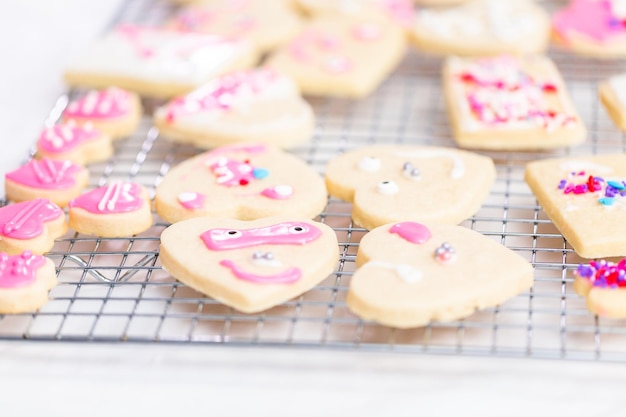 Decorating heart shape sugar cookies with royal icing and pink sprinkles for Valentine's day.