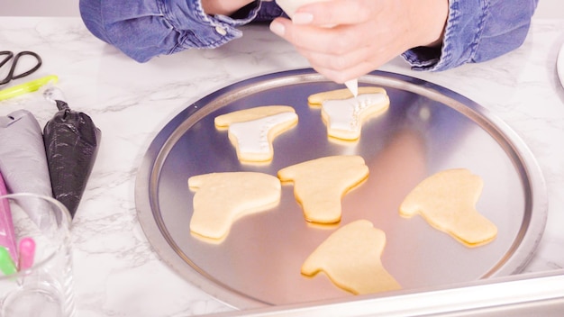 Decorating ice skate shaped sugar cookies with white color royal icing.