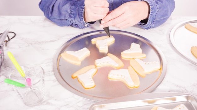 Decorating ice skate shaped sugar cookies with white color royal icing.