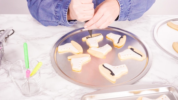 Decorating ice skate shaped sugar cookies with white color royal icing.