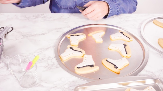 Decorating ice skate shaped sugar cookies with white color royal icing.