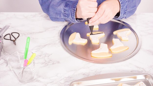 Decorating ice skate shaped sugar cookies with white color royal icing.