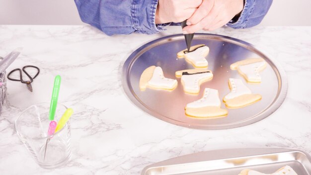 Decorating ice skate shaped sugar cookies with white color royal icing.