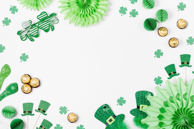 Decorations and props for St.Patrick 's Day party. Green and gold paper decorations, hat, balloons, confetti, candy and lucky symbols on white background. Festive concept. Flat lay, top view.